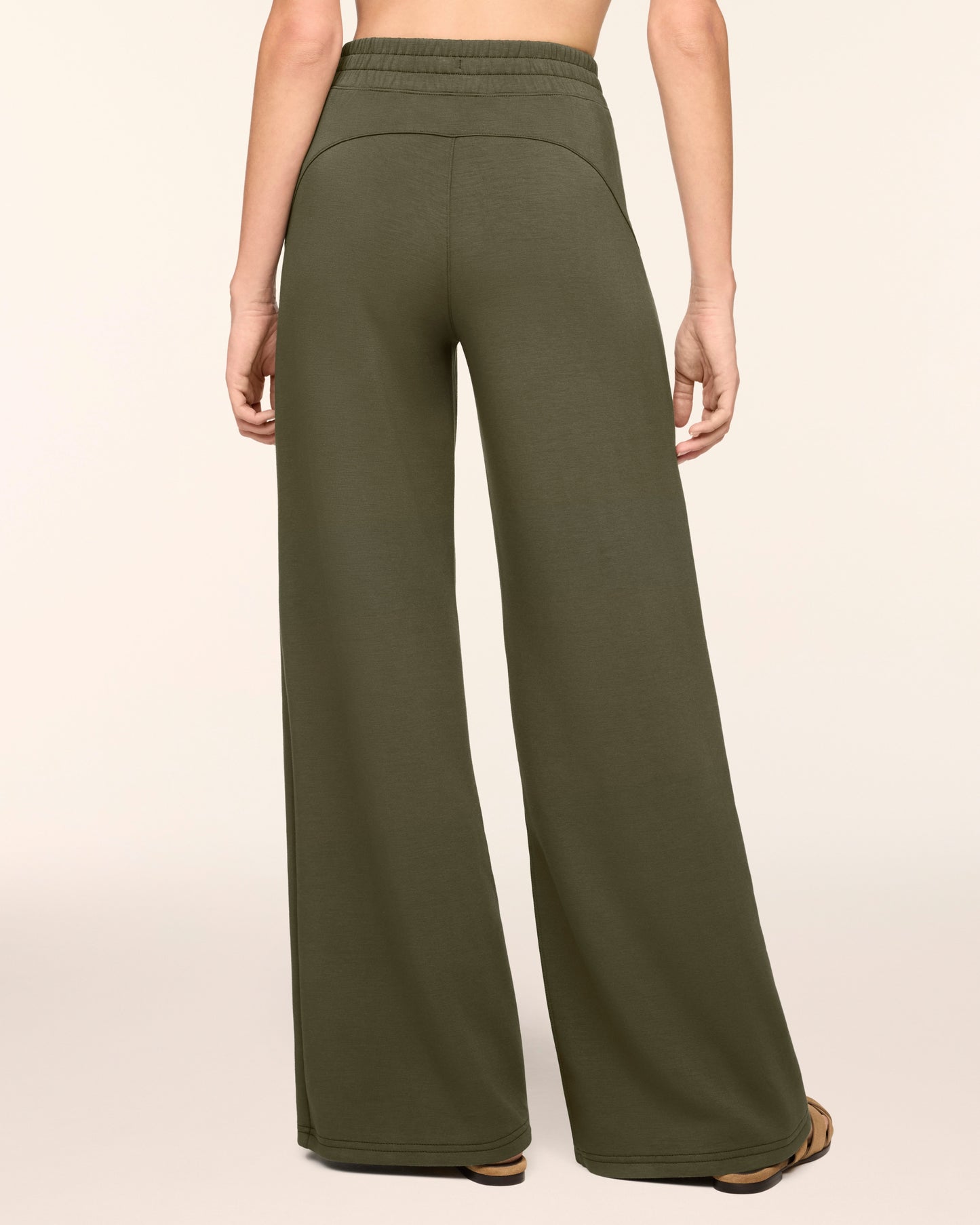 A person shown from the back wearing olive green wide-leg sweatpants against a plain light beige studio background.