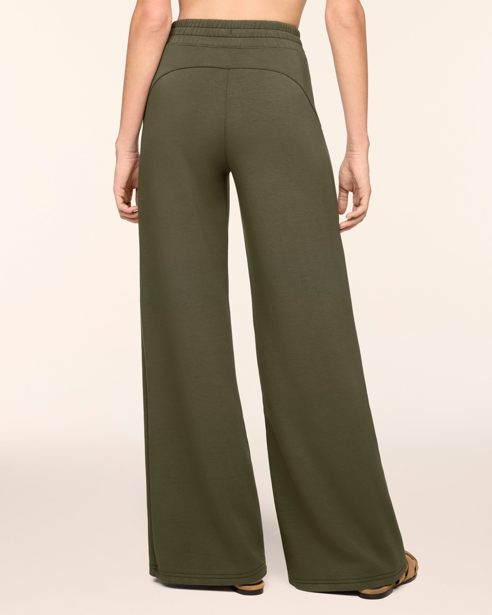 A person shown from the back wearing olive green wide-leg sweatpants against a plain light beige studio background.