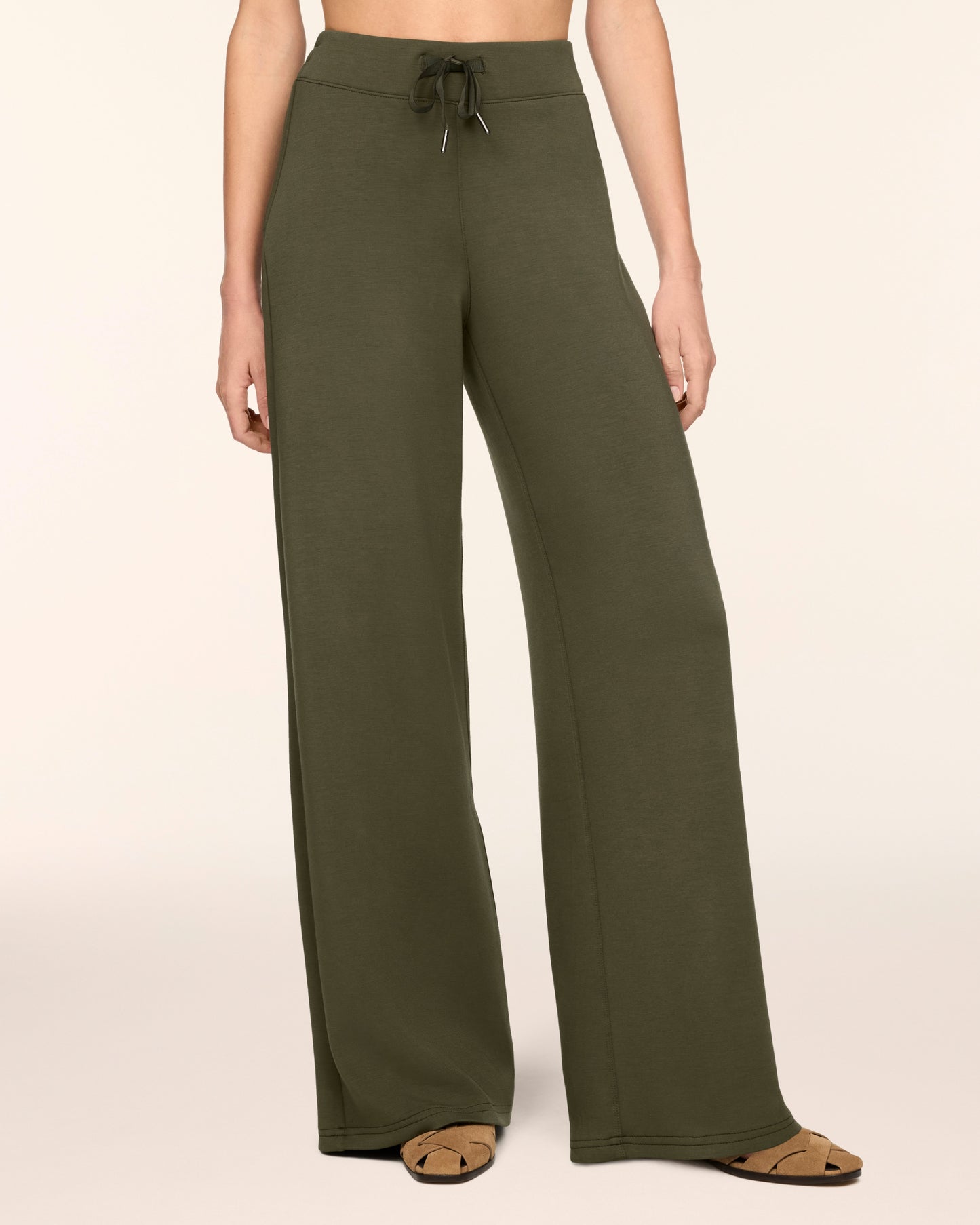 A model wearing olive green wide-leg lounge pants with a drawstring waistband, paired with brown flat sandals, against a solid cream background.