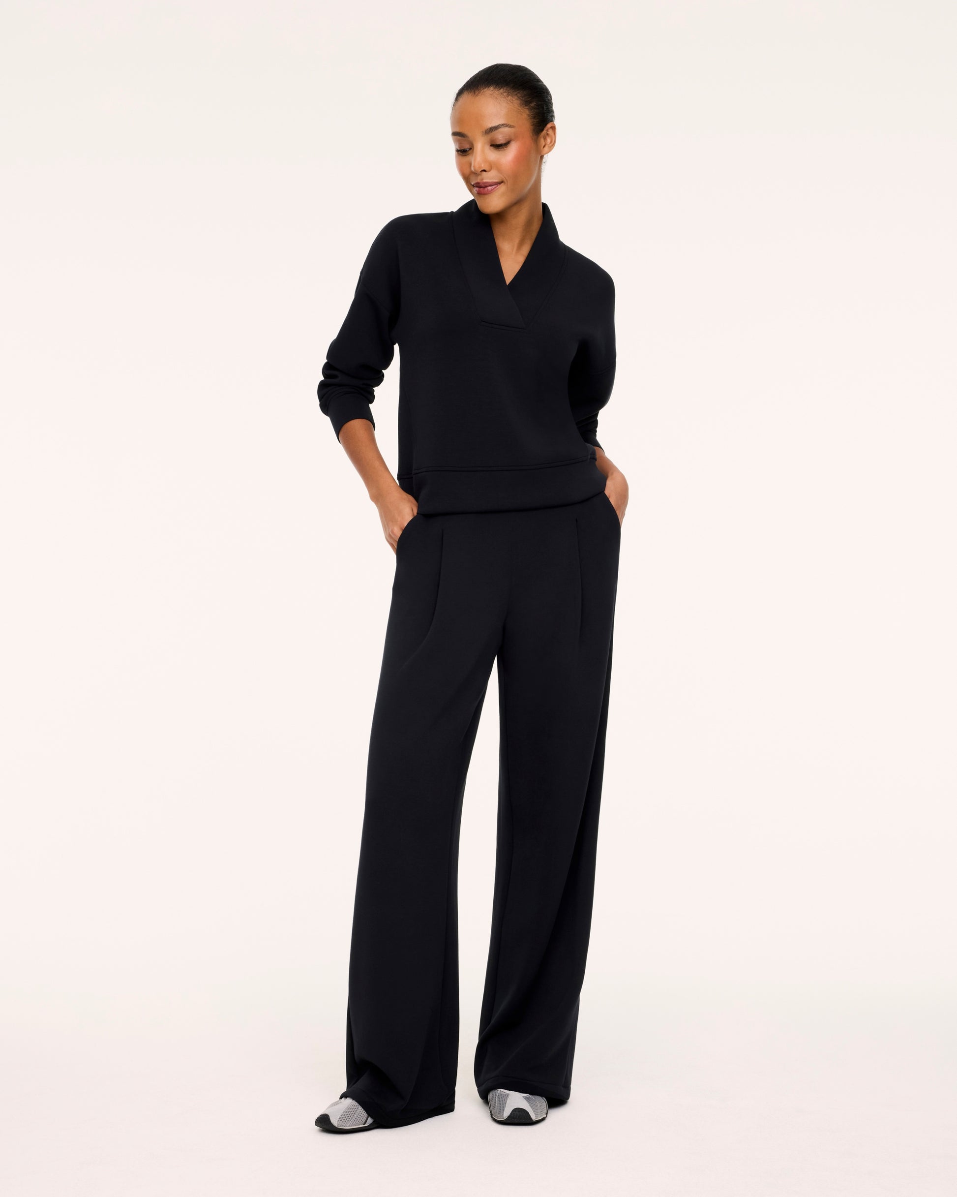 A woman modeling a black long-sleeve knit top and matching wide-leg trousers against a plain white studio background.