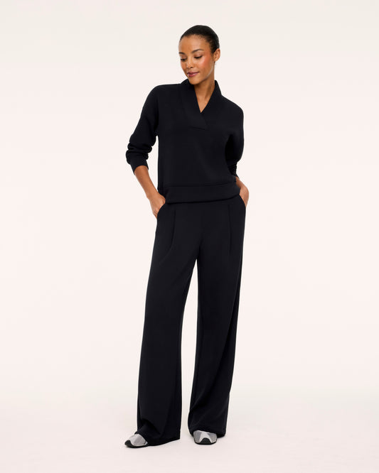 A woman modeling a black long-sleeve knit top and matching wide-leg trousers against a plain white studio background.
